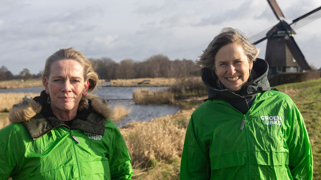 Annemarie van GroenLinks Oostzaan en Jacobien van Boeijen van GroenLinksLandsmeer staan buiten in het Twiske met hun groene campagne jasjes aan met op de achtergrond de Twiske Molen.